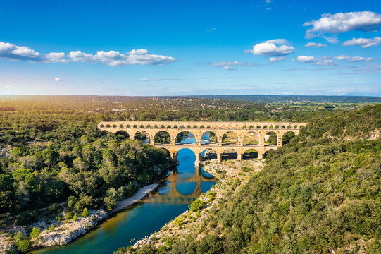 Aqueduct of Pont du Gard arches over the river, showcasing the rich history of Vers-Pont-du-Gard, France. Ancient aqueduct of Pont du Gard spans the peaceful river in Vers-Pont-du-Gard, France.