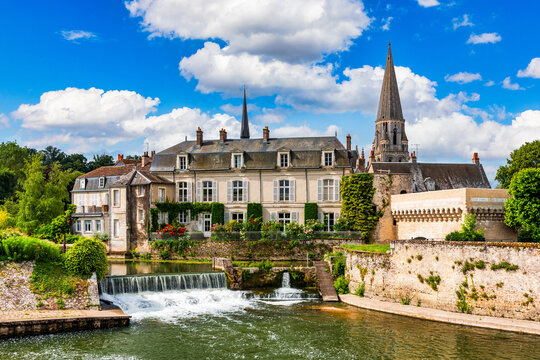 Vendome town, France, showcasing traditional architecture, the historic Trinity Abbey spire, and the scenic Loir River flowing under a bright blue sky with white clouds