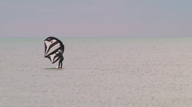 An athlete standing on the board holds on to the wing, in which the wind creates thrust in slow motion. Wingfoil board where a surfer glides through the water on a hydrofoil board..