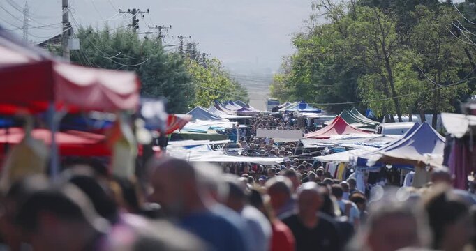 A busy outdoor market with crowd of people shopping and vendors selling their wares. The atmosphere is lively and bustling