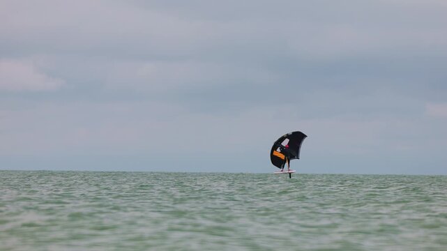 An athlete standing on the board holds on to the wing, in which the wind creates thrust in slow motion. Wingfoil board where a surfer glides through the water on a hydrofoil board..