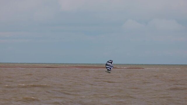 An athlete standing on the board holds on to the wing, in which the wind creates thrust in slow motion. Wingfoil board where a surfer glides through the water on a hydrofoil board..