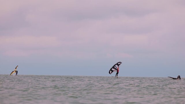 An athlete standing on the board holds on to the wing, in which the wind creates thrust in slow motion. Wingfoil board where a surfer glides through the water on a hydrofoil board..