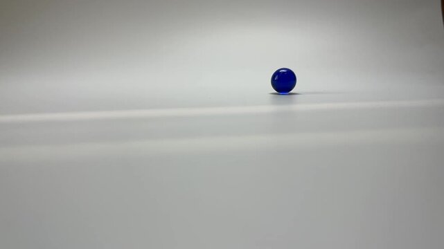 Collision of two glass balls and change in direction of motion. Two colored glass balls collide and bounce away from each other. Collision of colored glass balls demonstrating momentum transfer.