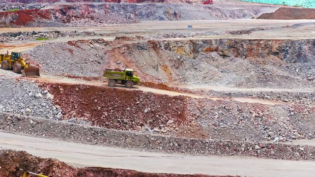 Aerial view of an open-pit mine with terraced rocky excavation, a yellow haul truck, layered earth, and diffuse overcast light.