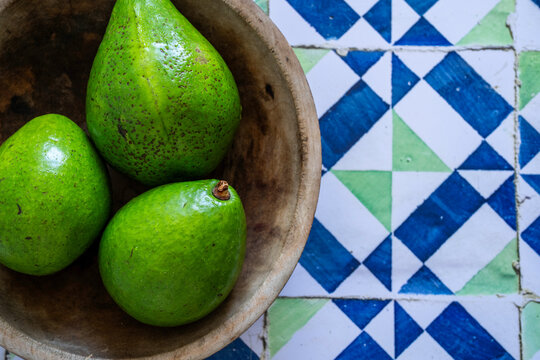 Avocados in a wood bowl on a tile surface 