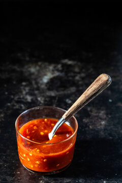 Chili paste in a container with a spoon on a dark surface 