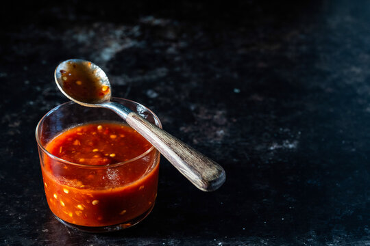 Chili paste in a container with a spoon on a dark surface 