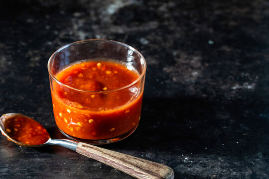 Chili paste in a container with a spoon on a dark surface 