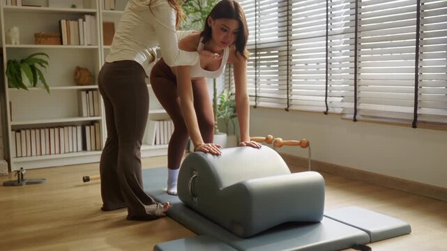 Pilates instructor guiding client through leg extension exercise on barrel, hands-on hip support for balance and alignment, personalized coaching session concept