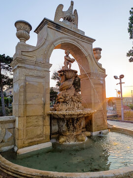 Ornamental Baroque fountain in The Mall garden with a cherub atop sculpted carp spilling water at sunset, Floriana MALTA