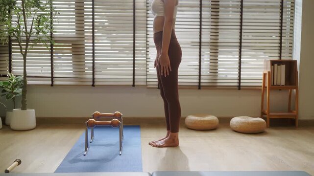 Woman stretching arm overhead standing by window, morning stretch routine with warm sunlight silhouette, side profile wellness and flexibility practice concept