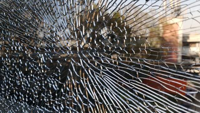 Dramatic close up of shattered glass with extensive radial cracks over a blurred urban street scene, creating a powerful visual metaphor for damage, vulnerability, impact and disruption