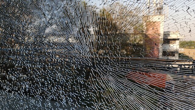 Dramatic close up of shattered glass with extensive radial cracks over a blurred urban street scene, creating a powerful visual metaphor for damage, vulnerability, impact and disruption