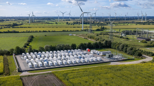 Aerial view of a large-scale battery energy storage system (BESS) surrounded by green fields and wind turbines in rural landscape, renewable energy infrastructure and sustainability concept.