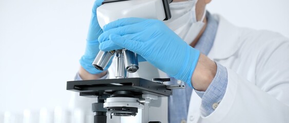 Scientist in a lab coat and protective gear precisely adjusting a microscope, conducting essential...