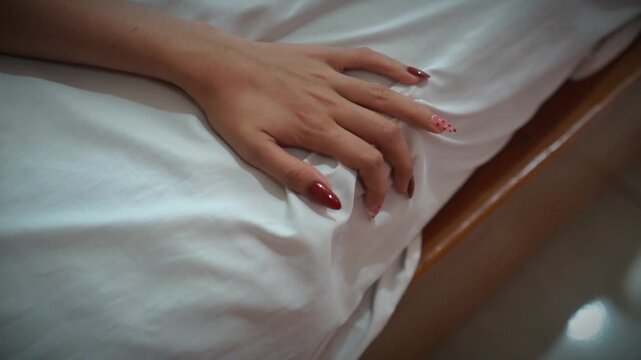 Close up of woman hand gripping bed sheets, concept of having sex on bed, experiencing menstrual cramps and period pain
