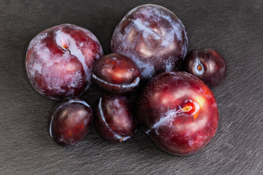 Plums different varieties and sizes on black flat slate plate