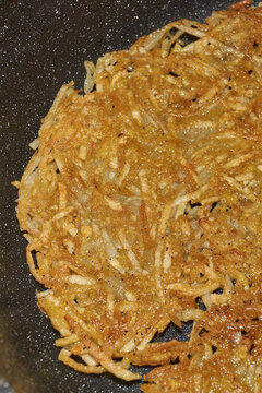 Large grated potato fritter cooking in a frying pan. Hot oil bubbles around the potato pancake as a golden crispy crust forms during frying. Homemade potato pancake made from coarsely grated potatoes.