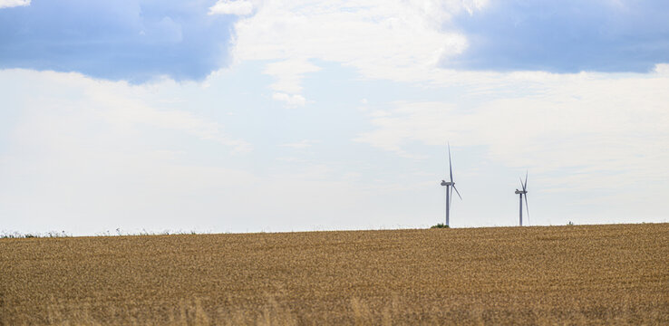 Two distant wind turbines rising beyond harvested agricultural field.