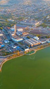 Vertical video. Russia, Votkinsk. Embankment with dam and factories, aerial panoramic view at sunset over the Votkinsk Reservoir, industrial waterfront and golden evening light. Drone footage. Rich c