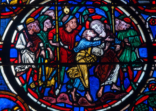 Judas kisses Jesus while armed men surround them on a colorful Gothic stained glass panel.