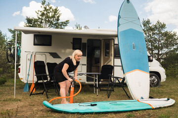 A woman inflates a sup-board for swimming near her motorhome © Alex