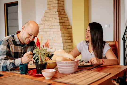 Couple enjoying a relaxed breakfast at home, with the man looking down at his meal while his partner smiles and interacts with him.