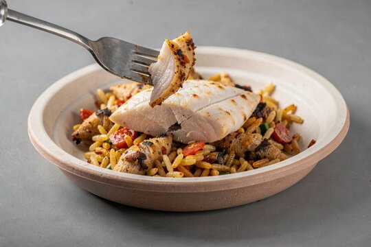 Bowl of Mutabbaq Samak featuring grilled fish, rice, onions, spices, topped with colorful vegetables. Concept of flavorful dish emphasizing fish with rice onions spices.