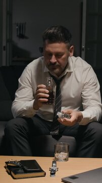Vertical video of middle aged Caucasian businessman opening decanter and pouring whiskey into glass. Footage represents burnout, work stress, mental health and addiction awareness