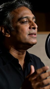 Vertical video: Singing on recording cue, man in dark shirt in vocal booth with mic and pop filter