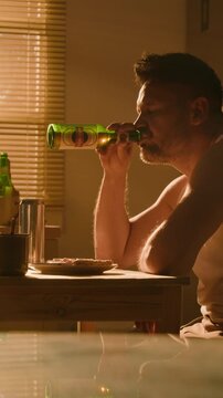 Vertical video of middle aged Caucasian man drinking beer and holding head in despair. Footage suitable for mental health campaigns, addiction recovery, and depression awareness