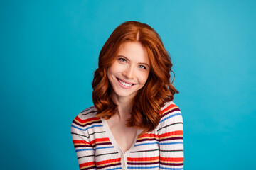 Fototapeta premium Smiling redhead woman portrait wearing a striped sweater against a blue background, cheerful headshot conveying happiness, warmth and approachable beauty