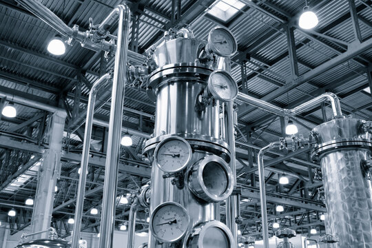 Stainless steel towers dominate the factory interior. Pressure gauges monitor  industrial processes. Pipes connect metal structures throughout space