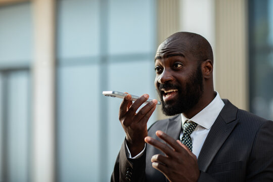 Businessman using voice assistant on smartphone outdoors