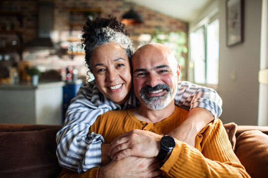 Smiling mature couple hugging on sofa at home