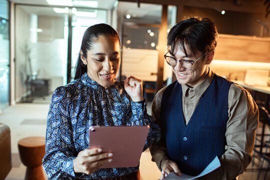 Two coworkers celebrating success on tablet in modern office