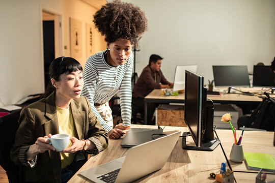 Two coworkers collaborating at computer in modern open-plan office