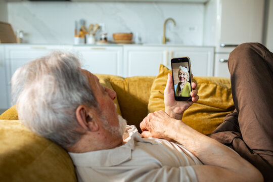 Senior man video calling loved one on sofa at home