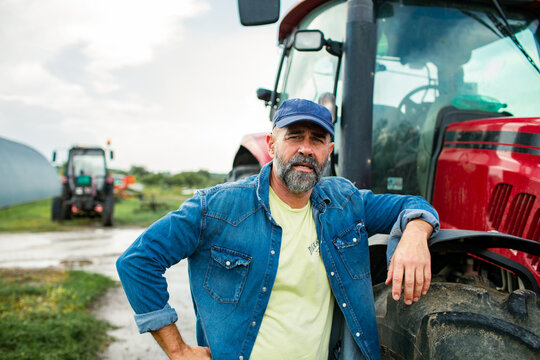 Middle-aged farmer leaning on red tractor outdoors