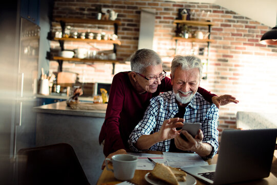 Senior couple using smartphone for online banking in kitchen