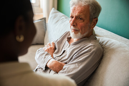 Senior man talking with caregiver on sofa at home