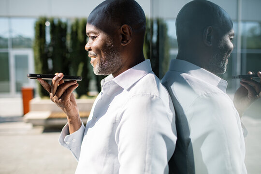 Smiling mature man using smartphone voice commands outside office building