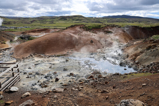 Steam rises from a turquoise hot spring pool between mineral-colored slopes at Seltun geothermal area, Reykjanes, Iceland.