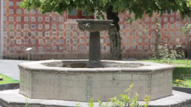A richly decorated interior courtyard showcases traditional Mexican architecture through a sculpted stone fountain, exposed brickwork, graceful architectural details, and Talavera Poblana tiles.