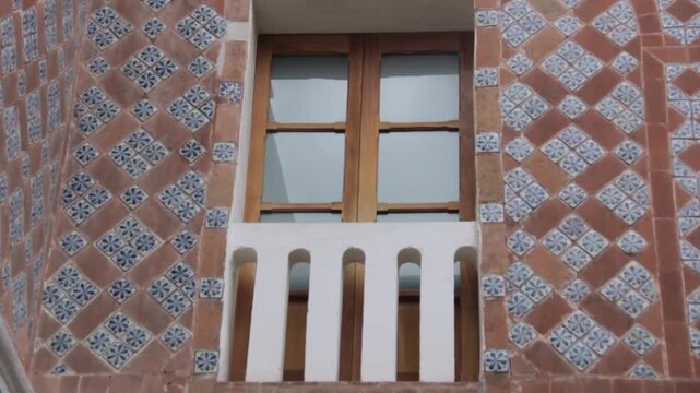 A traditional wooden window stands within an ornate Baroque facade covered with colorful Talavera Poblana tiles, evoking the architectural details of everyday life in historic Mexico.