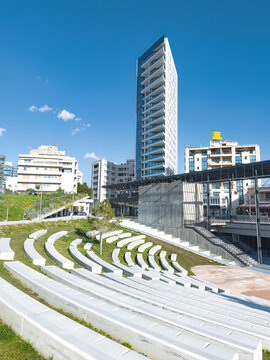 Modern urban park with white amphitheater seating and a tall building in GSP Square. Nicosia, Cyprus