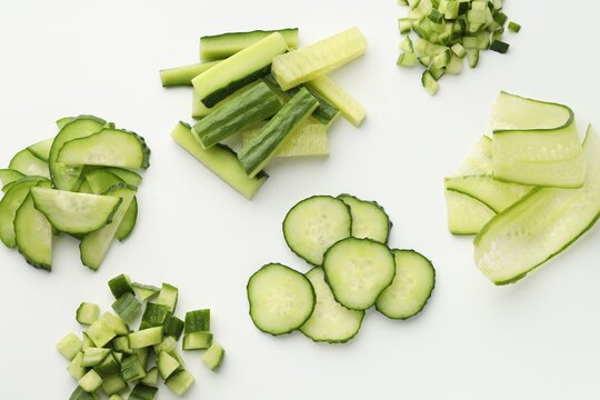 Different cuts of cucumbers on white background, flat lay