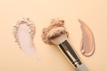 Swatches of foundation, face powders and brush on beige background, flat lay