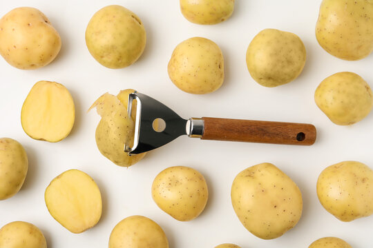Ripe young potatoes and peeler on white background, flat lay